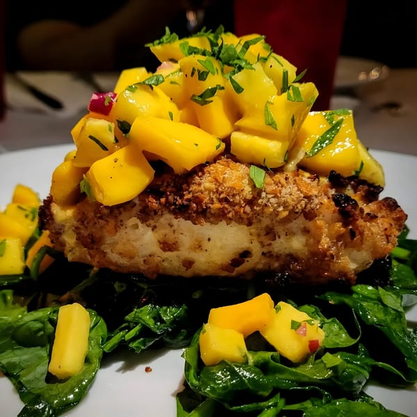 Leone's Italian dish with breaded fish, mango salsa, and spinach on a white plate.