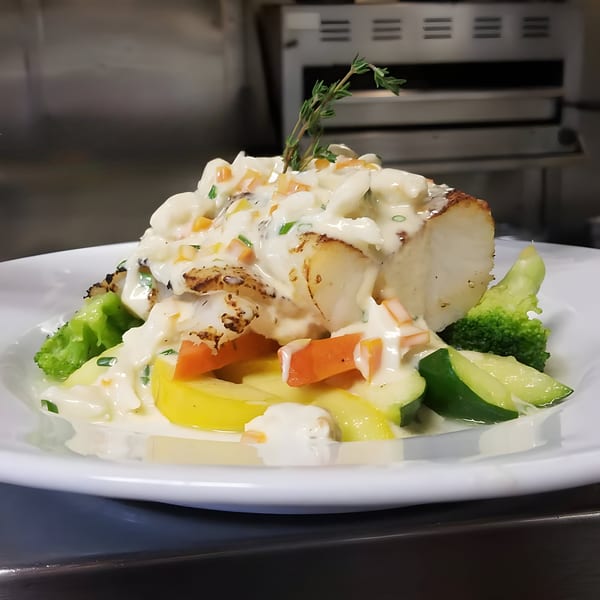 Seared fish topped with creamy sauce, diced vegetables, and fresh herbs, served with broccoli and zucchini.